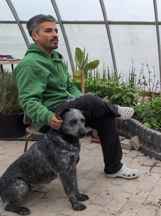 Antonio Gomes, founder of VillageWorksOS, in the greenhouse with his dog